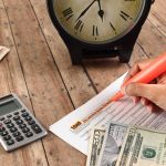 hand highlighting tax form with calculator and clock